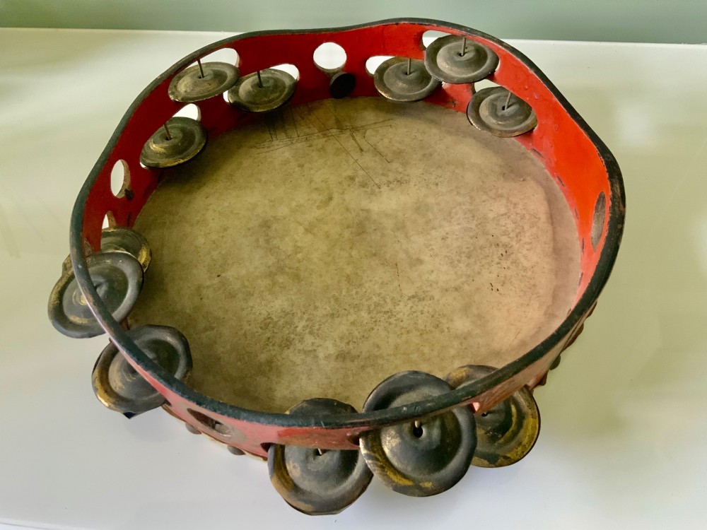An antique Regency circular wooden tambourine featuring hand-painted red and gold floral patterns, metal jingles set into the rim, and a taut vellum head secured with brass studs. View III
