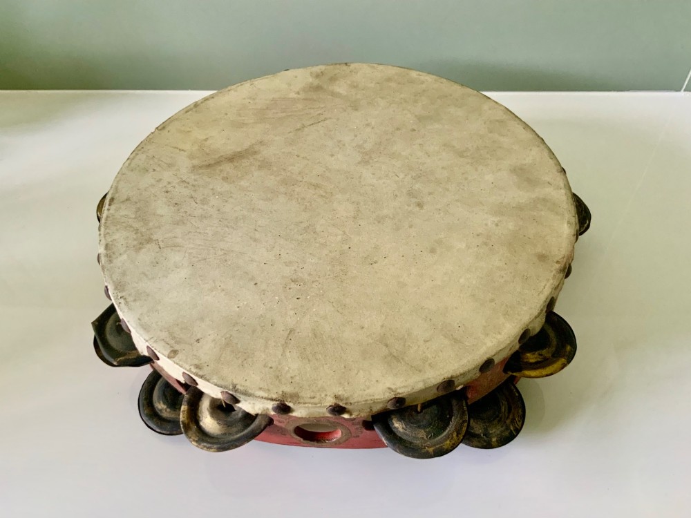 An antique Regency circular wooden tambourine featuring hand-painted red and gold floral patterns, metal jingles set into the rim, and a taut vellum head secured with brass studs. View IV