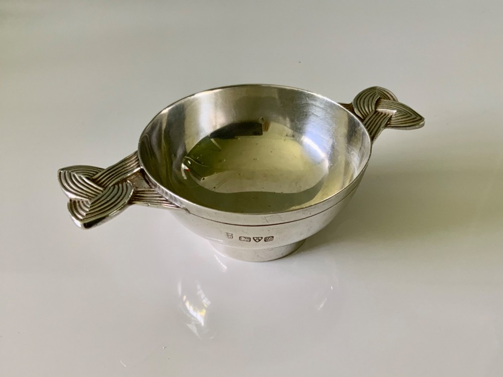 A shallow sterling silver quaich featuring two textured Celtic knot handles and visible hallmark stamps on the outer bowl.