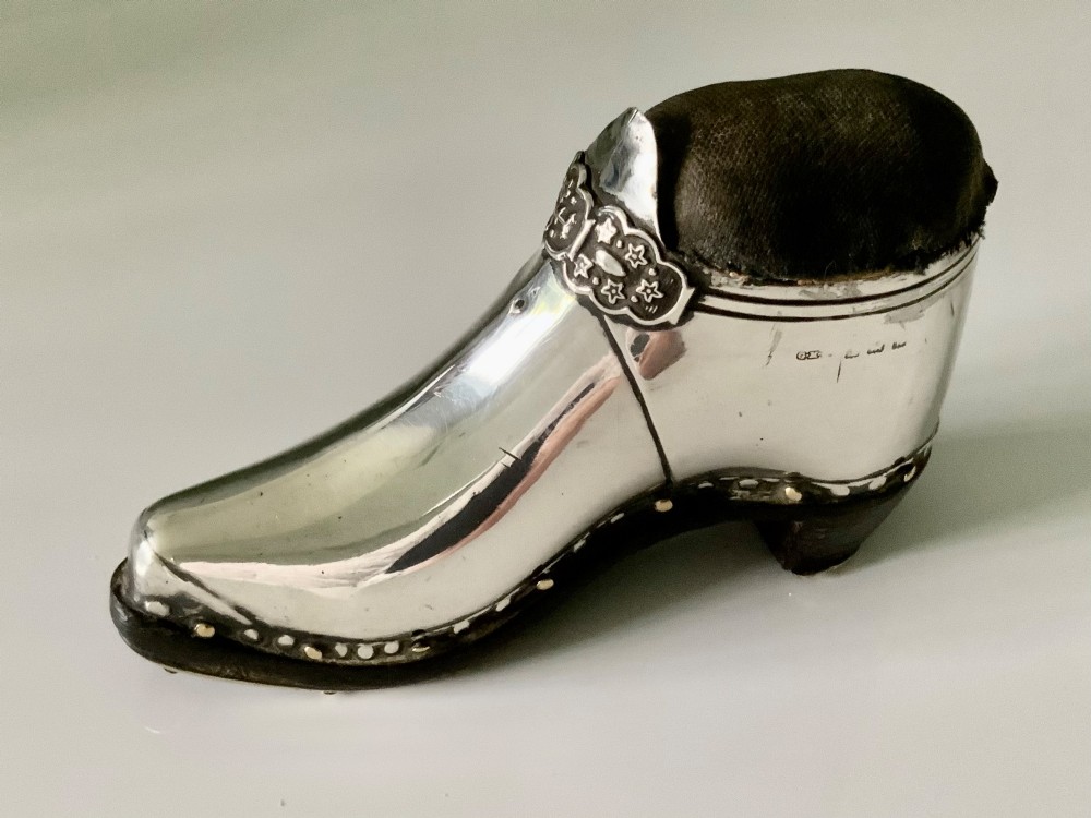 An antique sterling silver pin cushion crafted in the shape of a clog shoe with a dark velvet pad and visible hallmarks.