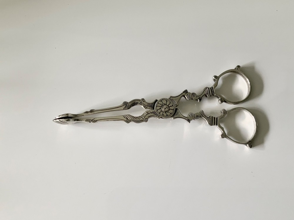 A pair of Georgian-style silver scissor-action sugar tongs with chased engraving and shell-shaped grips against a neutral background. View II