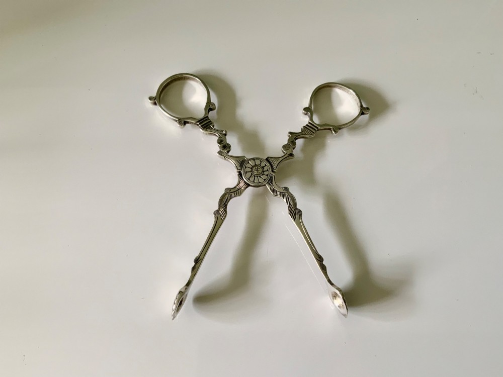 A pair of Georgian-style silver scissor-action sugar tongs with chased engraving and shell-shaped grips against a neutral background. View III