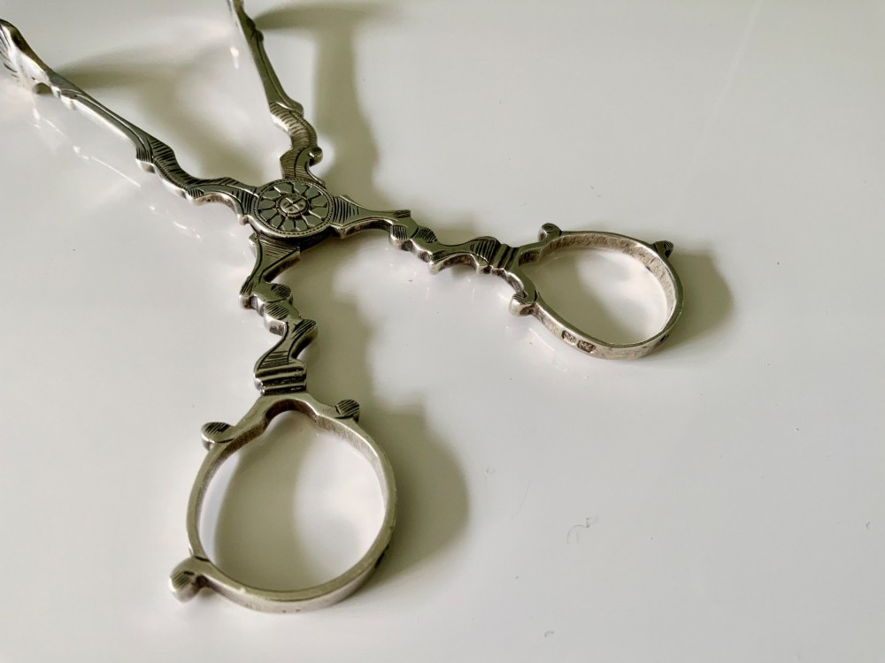 A pair of Georgian-style silver scissor-action sugar tongs with chased engraving and shell-shaped grips against a neutral background. View IV