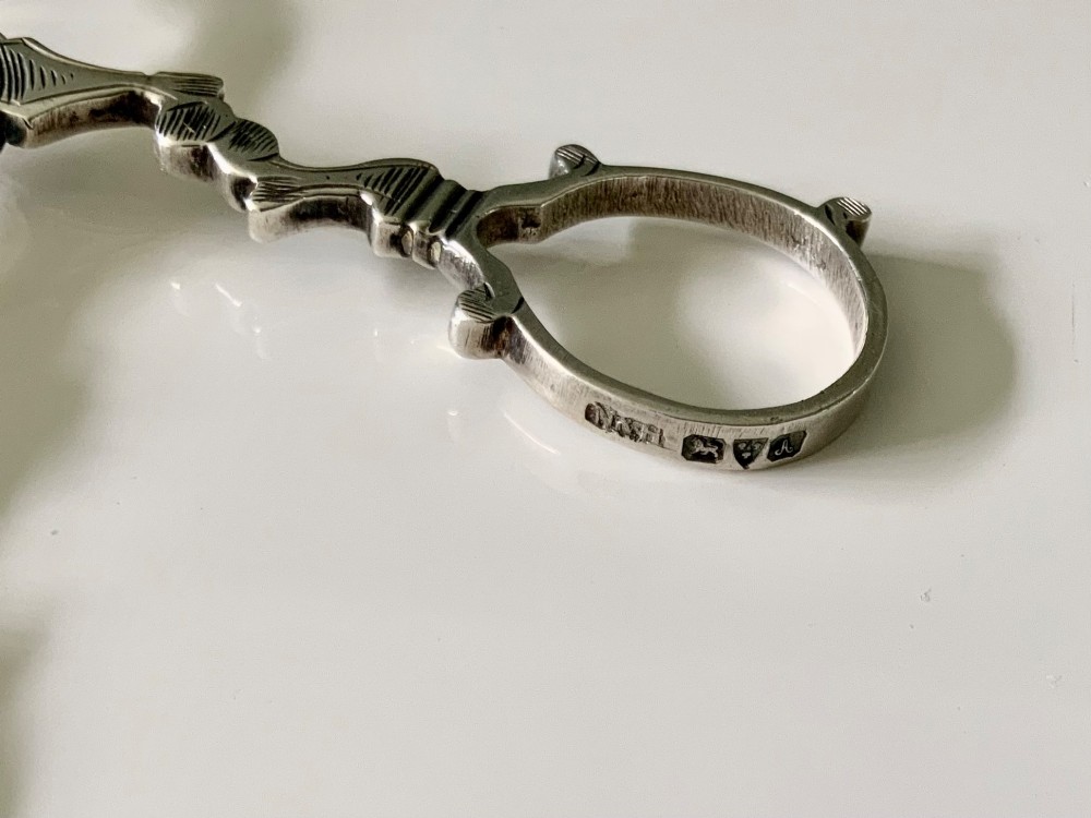 A pair of Georgian-style silver scissor-action sugar tongs with chased engraving and shell-shaped grips against a neutral background. View V