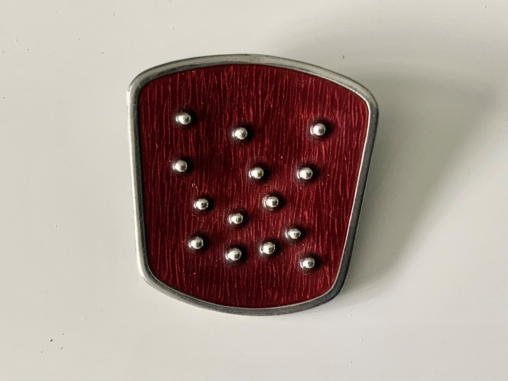 A shield-shaped silver brooch featuring textured red translucent enamel decorated with small raised silver spheres.
