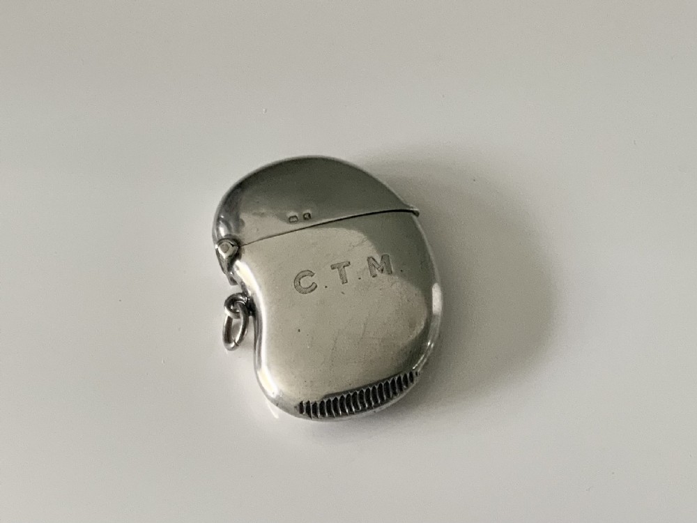 A kidney-shaped sterling silver vesta case featuring engraved monogram initials, a side suspension loop, and a serrated striking strip on the bottom edge.