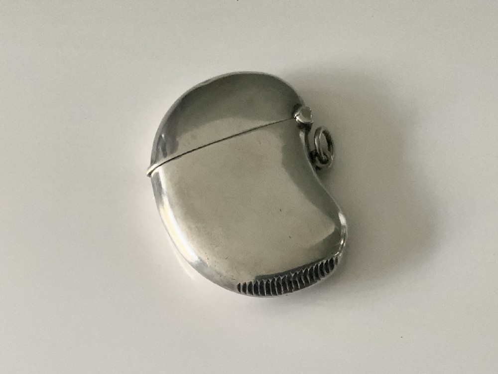 A kidney-shaped sterling silver vesta case featuring engraved monogram initials, a side suspension loop, and a serrated striking strip on the bottom edge. View II