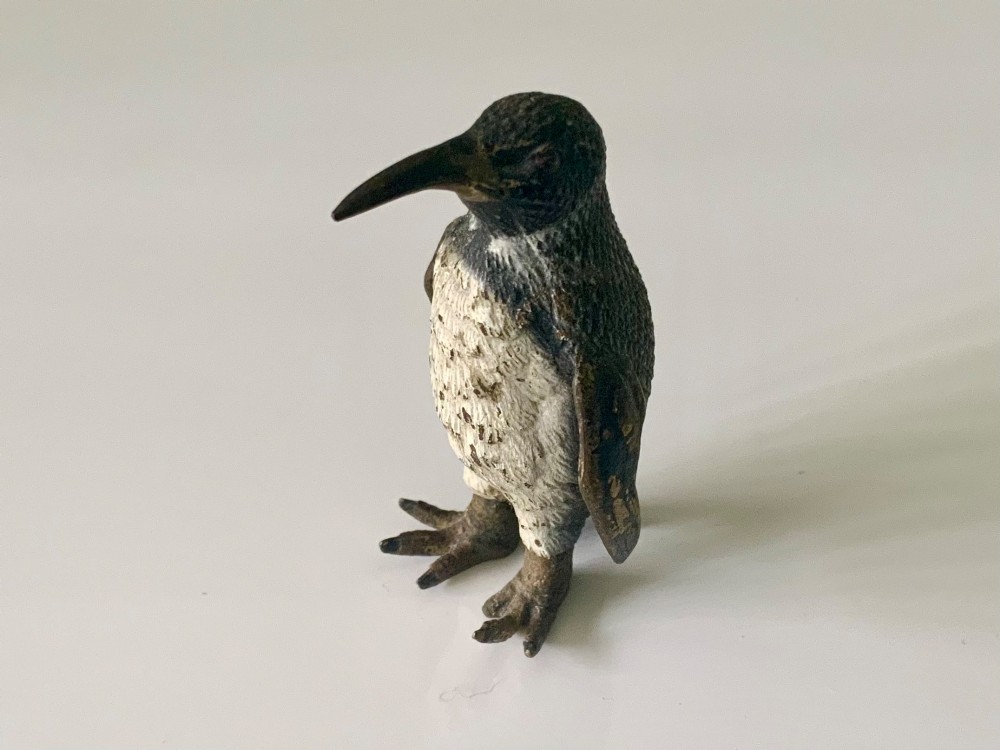 A small cold-painted bronze figurine depicting a standing penguin with textured feather details in dark brown, black, and off-white paint.