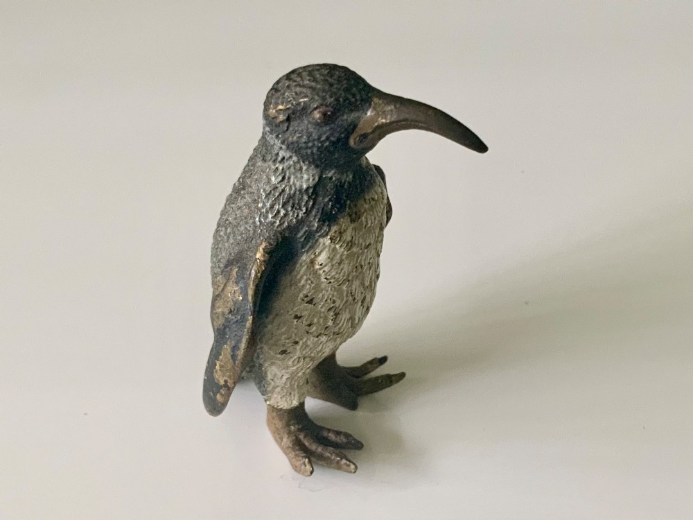 A small cold-painted bronze figurine depicting a standing penguin with textured feather details in dark brown, black, and off-white paint. View II