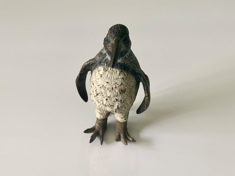 A small cold-painted bronze figurine depicting a standing penguin with textured feather details in dark brown, black, and off-white paint. View III