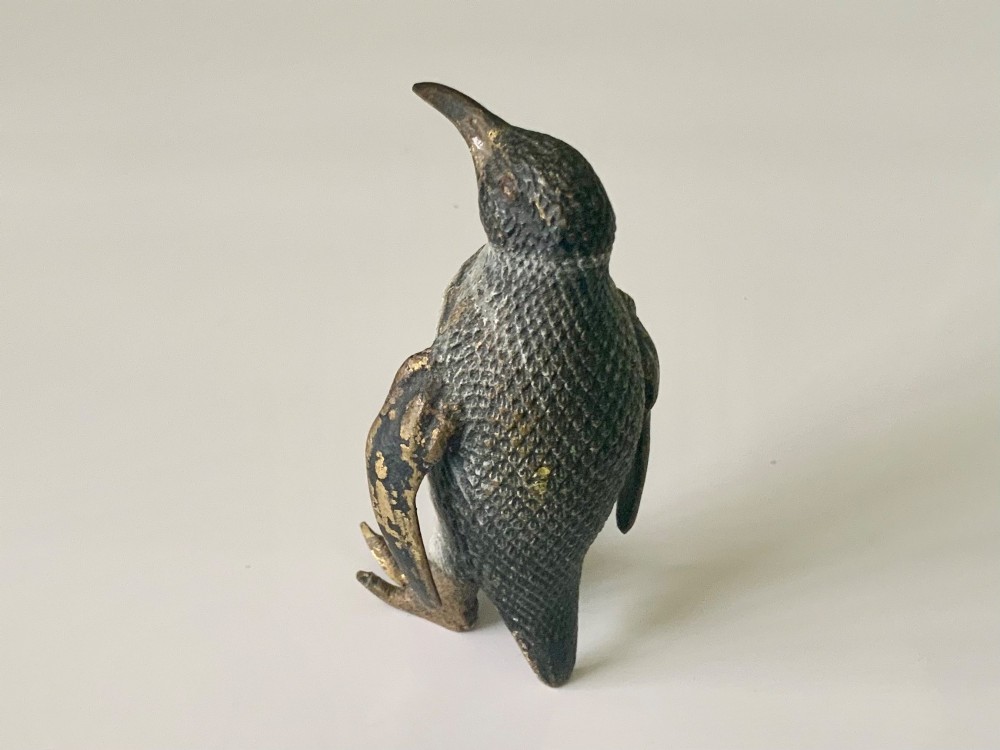 A small cold-painted bronze figurine depicting a standing penguin with textured feather details in dark brown, black, and off-white paint. View V