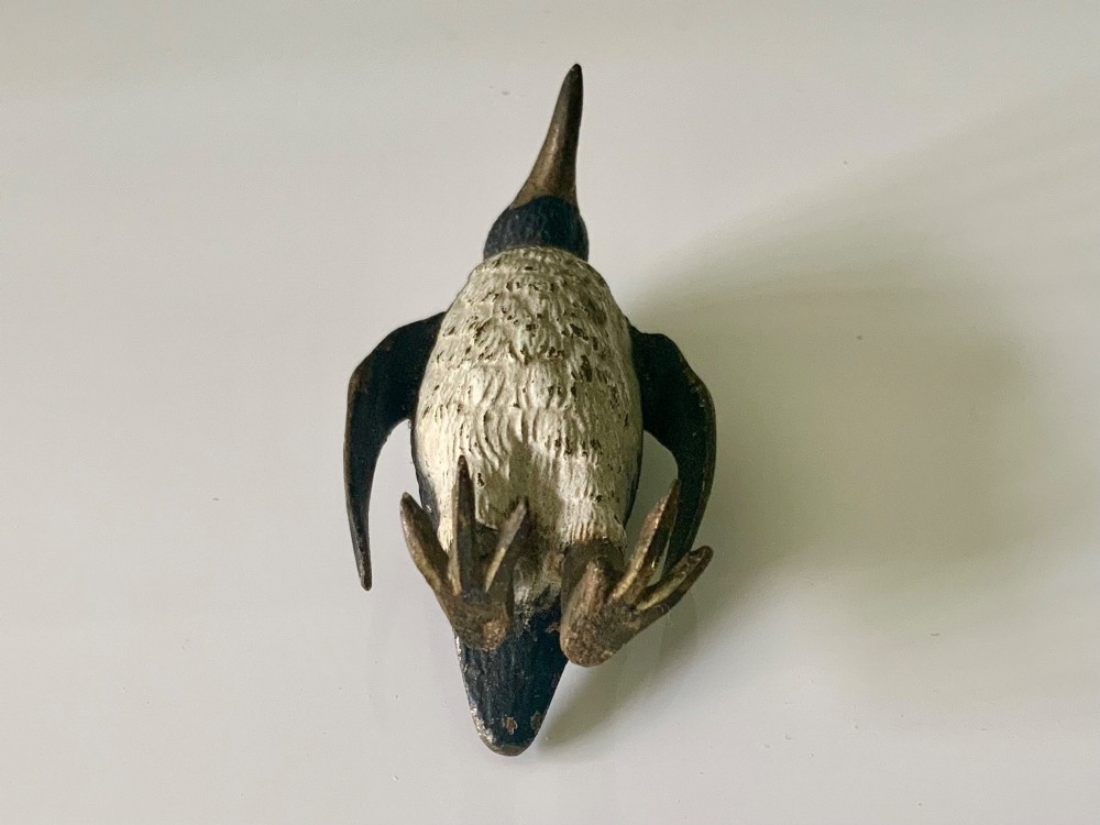A small cold-painted bronze figurine depicting a standing penguin with textured feather details in dark brown, black, and off-white paint. View VI
