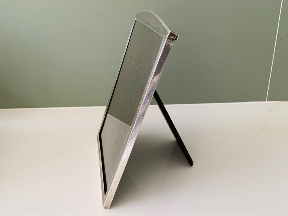 An Art Deco silver photo frame with a textured engine-turned border, an arched top profile, and a dark wooden interior backing. View II