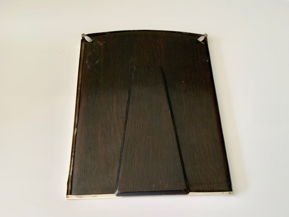 An Art Deco silver photo frame with a textured engine-turned border, an arched top profile, and a dark wooden interior backing. View V