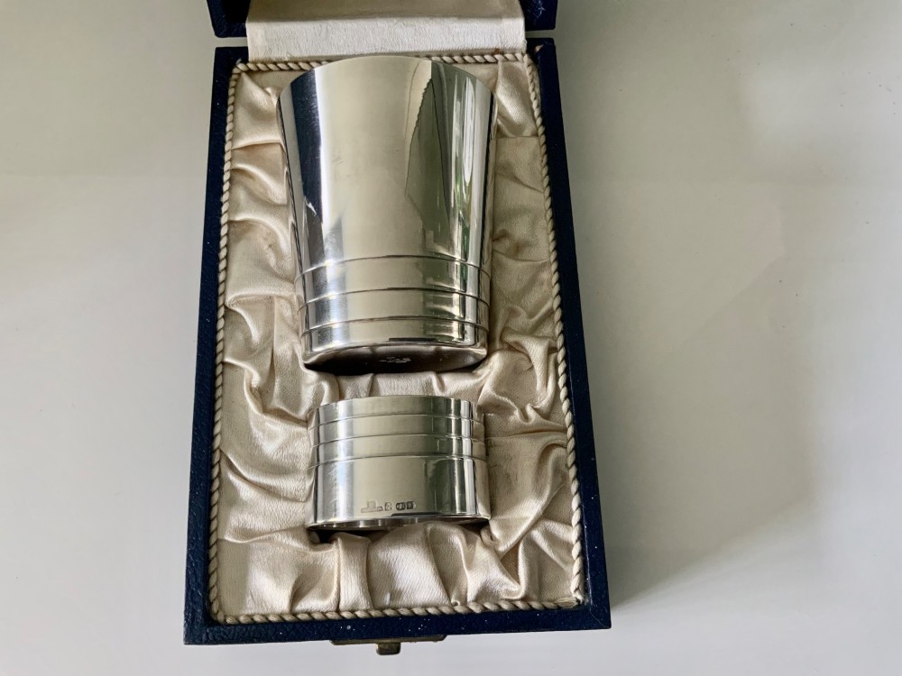 A silver-plated beaker and matching napkin ring with horizontal ridge details sit inside a blue presentation box lined with cream satin. View II