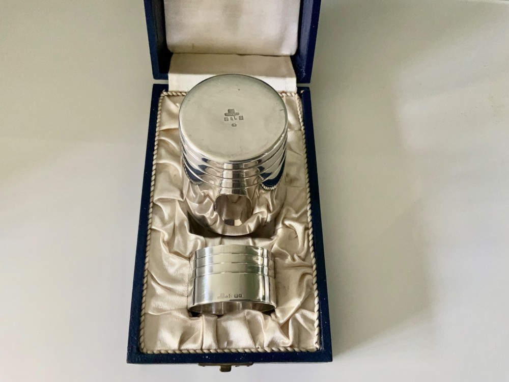 A silver-plated beaker and matching napkin ring with horizontal ridge details sit inside a blue presentation box lined with cream satin. View III
