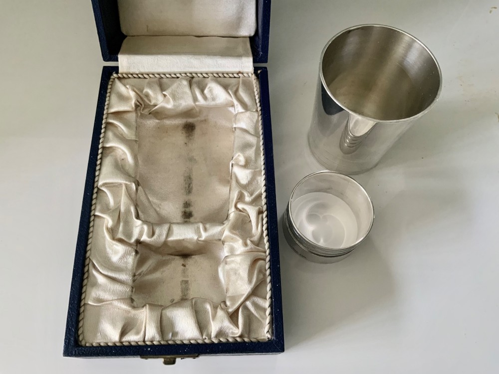 A silver-plated beaker and matching napkin ring with horizontal ridge details sit inside a blue presentation box lined with cream satin. View IV