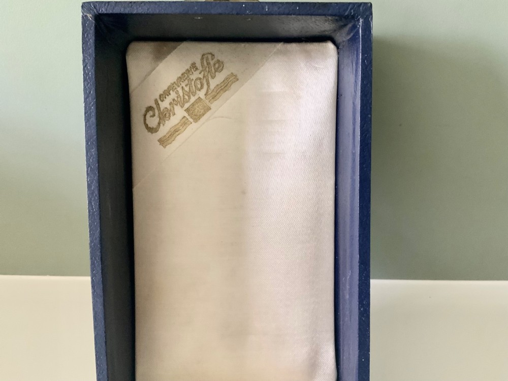 A silver-plated beaker and matching napkin ring with horizontal ridge details sit inside a blue presentation box lined with cream satin. View V