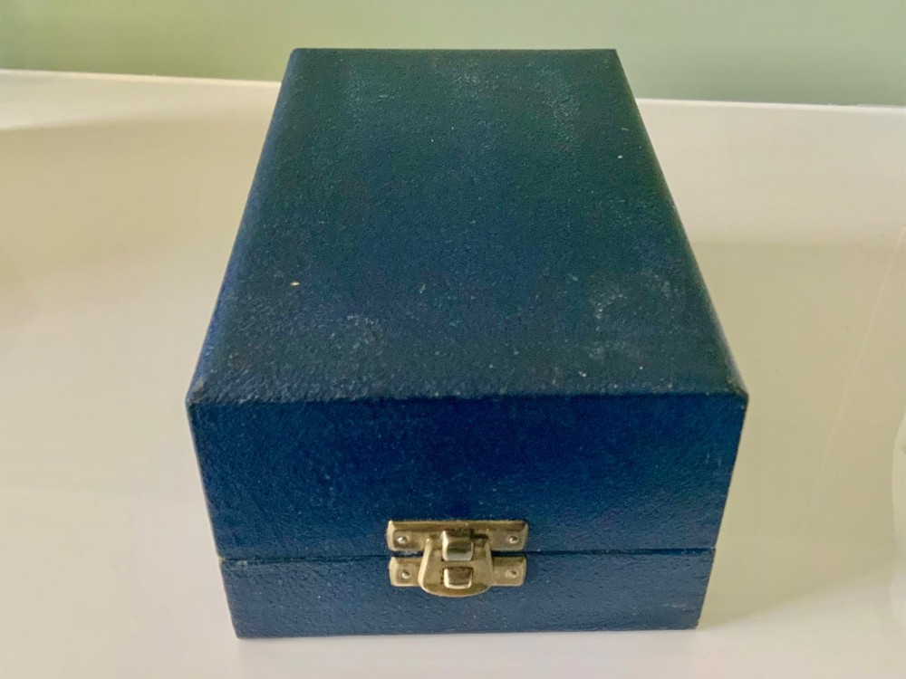 A silver-plated beaker and matching napkin ring with horizontal ridge details sit inside a blue presentation box lined with cream satin. View VI