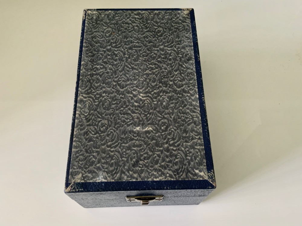 A silver-plated beaker and matching napkin ring with horizontal ridge details sit inside a blue presentation box lined with cream satin. View VII