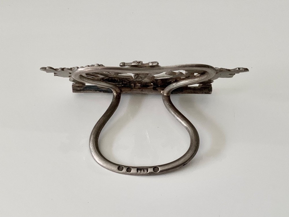 A cast silver menu holder featuring a central monkey figure playing drums framed by foliate scrollwork. View II