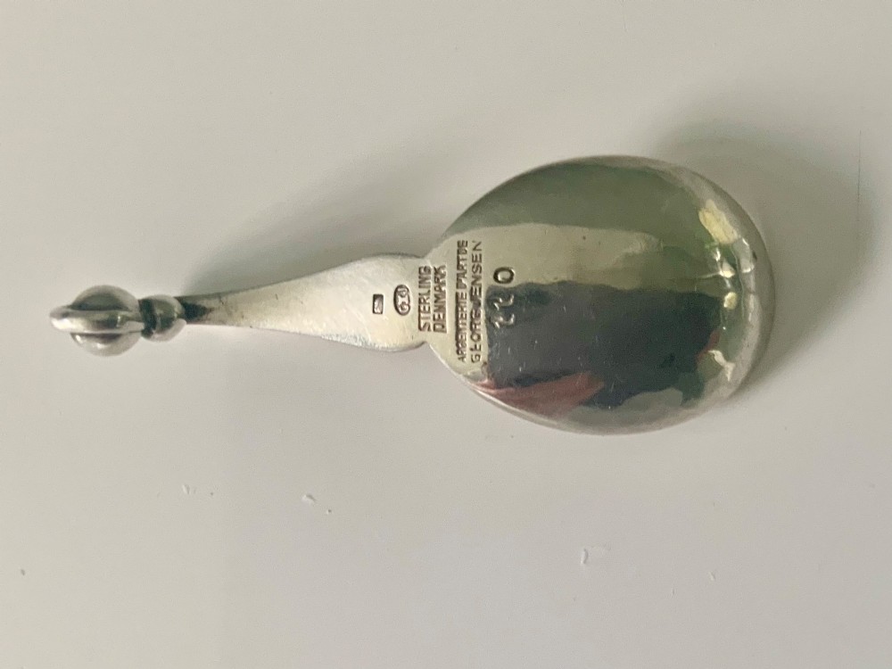 A Georg Jensen sterling silver open salt cellar with a curved handle and small spherical feet, containing a matching silver salt spoon. View II