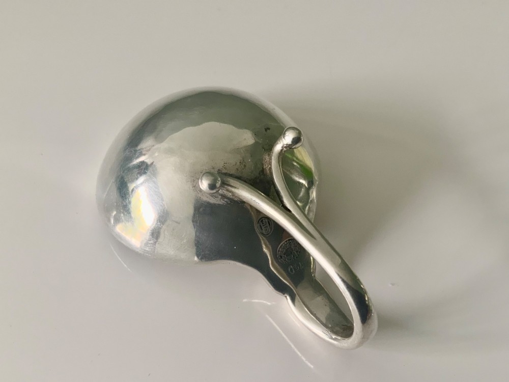 A Georg Jensen sterling silver open salt cellar with a curved handle and small spherical feet, containing a matching silver salt spoon. View VI