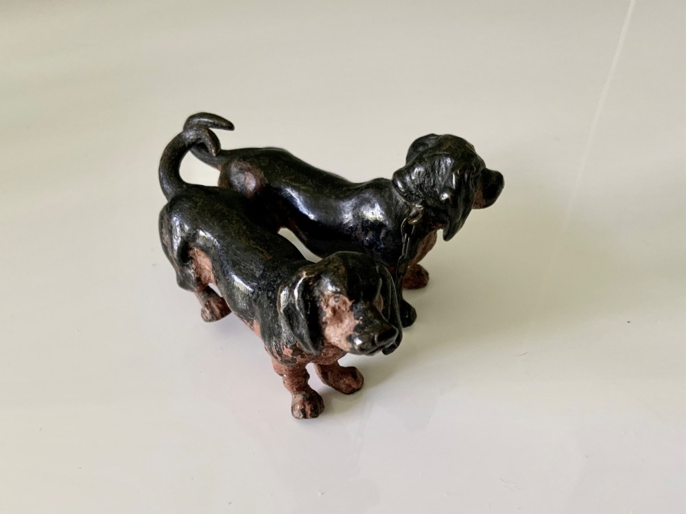 A pair of miniature black and tan cold-painted bronze dachshund figurines connected by a delicate metal chain. View II