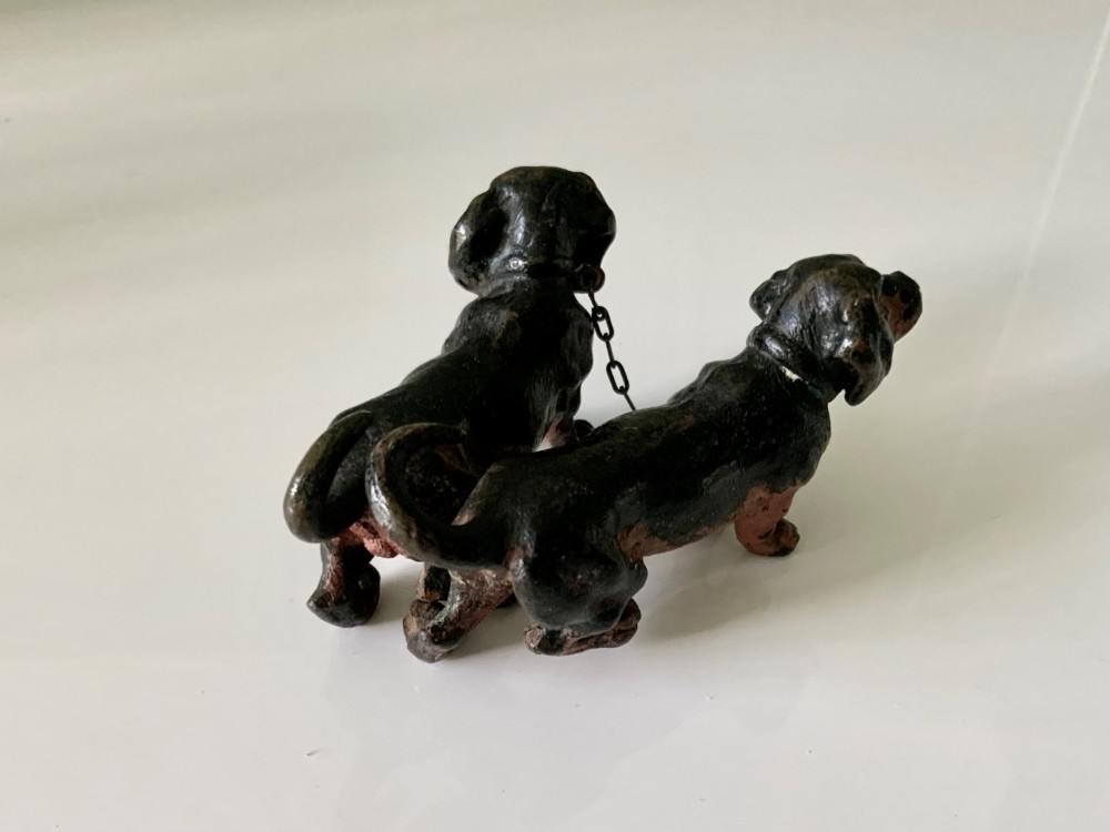 A pair of miniature black and tan cold-painted bronze dachshund figurines connected by a delicate metal chain. View V