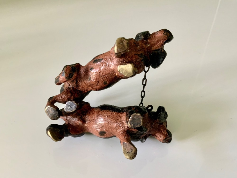 A pair of miniature black and tan cold-painted bronze dachshund figurines connected by a delicate metal chain. View VI