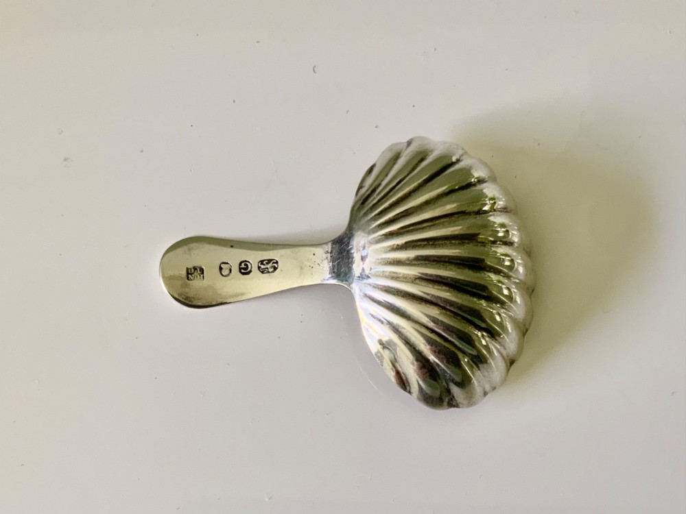 A Georgian sterling silver caddy spoon with a fluted shell-shaped bowl and a short bright-cut engraved handle. View II