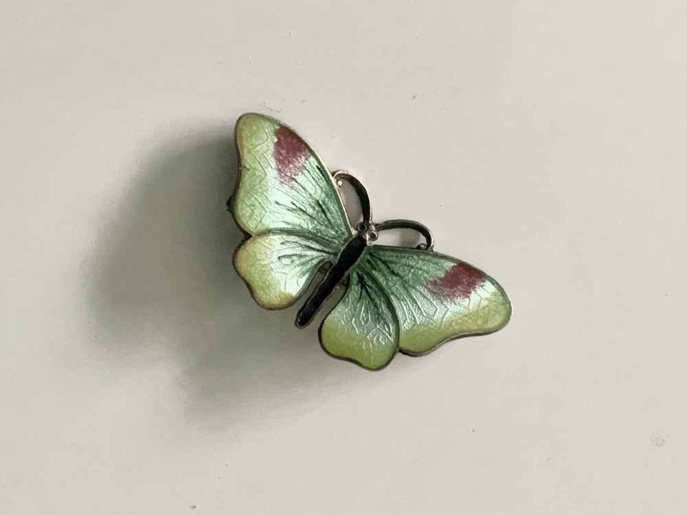 A silver brooch designed as a butterfly with pale green guilloche enamel wings edged in burgundy.