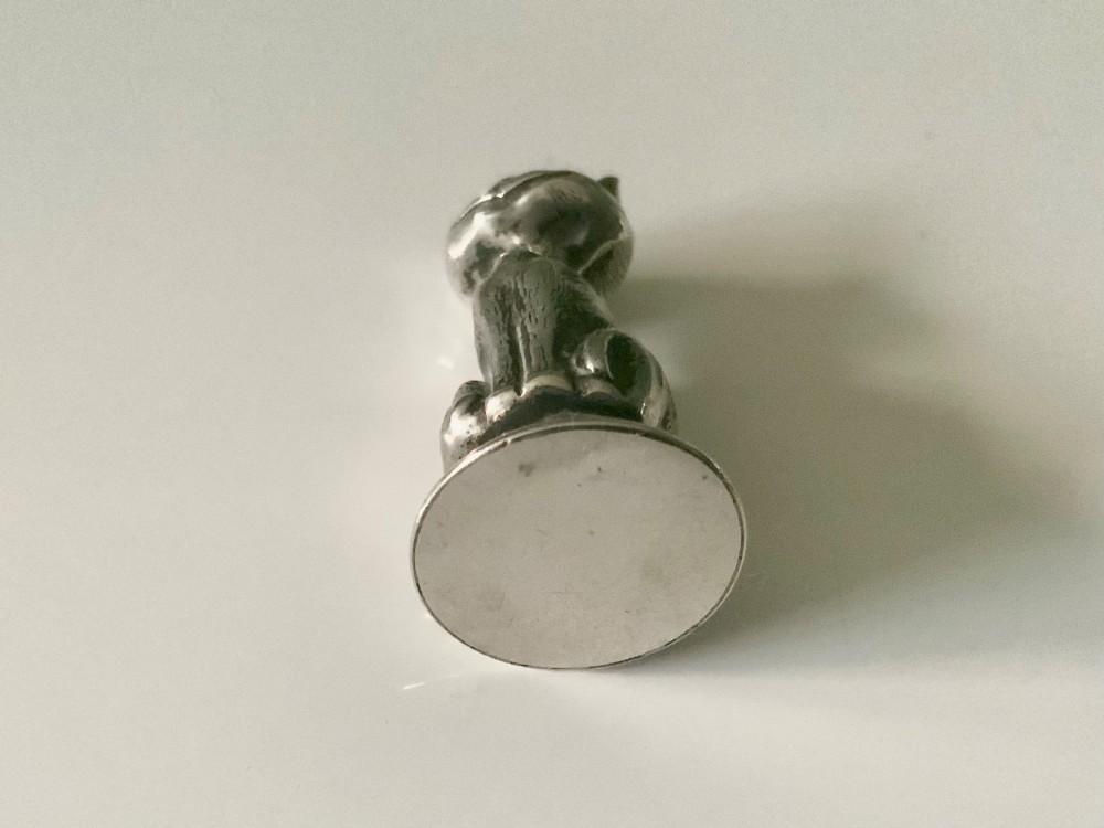 A small cast sterling silver figurine of a smiling Cheshire cat seated on a rounded wax seal base. View III