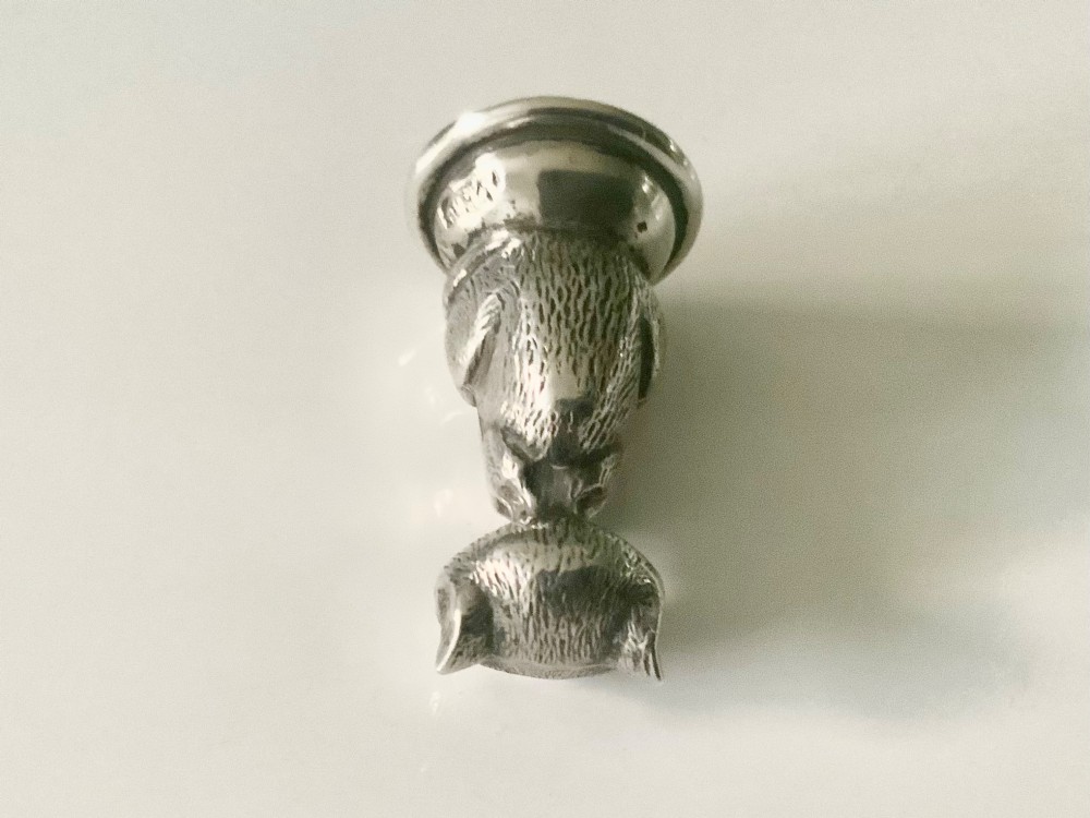 A small cast sterling silver figurine of a smiling Cheshire cat seated on a rounded wax seal base. View IV