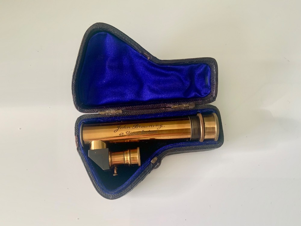 A nineteenth-century engraved brass pocket spectroscope resting inside an open fitted black leather case lined with bright blue velvet.