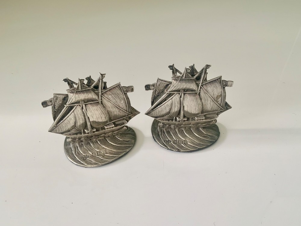 A pair of silver menu holders cast in the shape of three-masted galleon ships set atop ocean wave bases featuring stamped hallmarks.