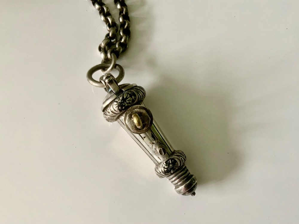 A silver-plated military whistle with fluted details connected by a metal link chain to a circular lion mask boss mount. View IV