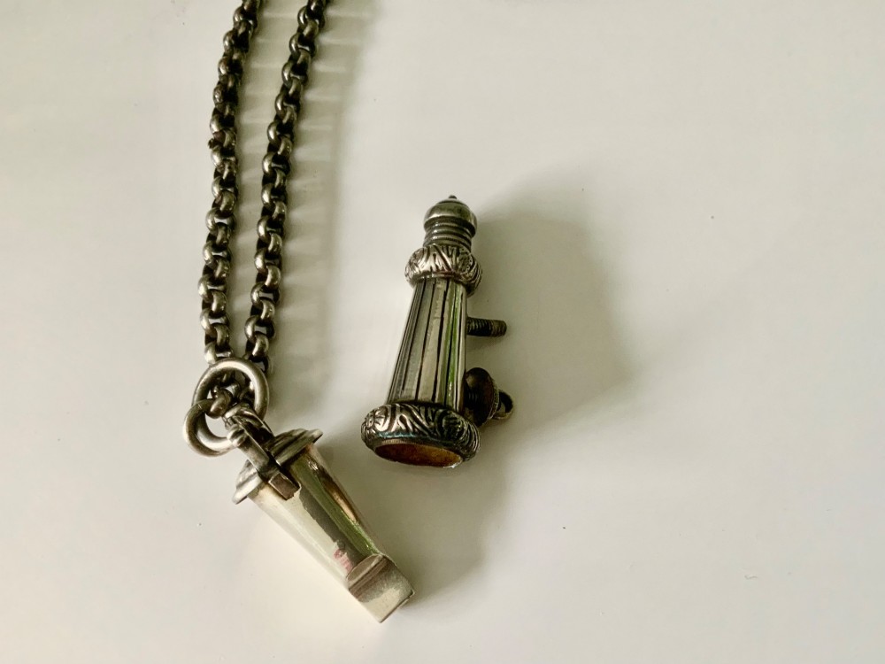 A silver-plated military whistle with fluted details connected by a metal link chain to a circular lion mask boss mount. View VI