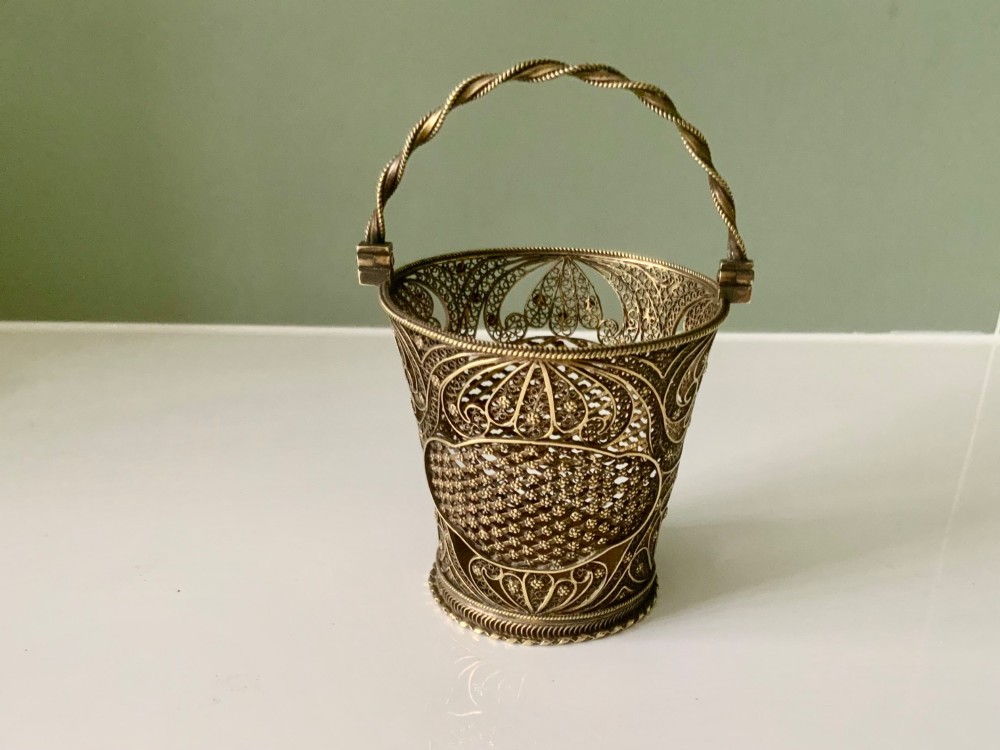 A small cylindrical silver gilt filigree basket with a twisted swing handle and intricate openwork lacelike patterns.