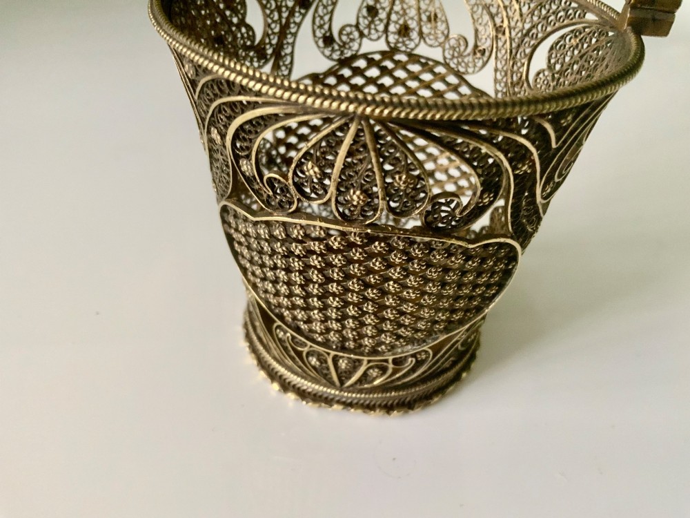 A small cylindrical silver gilt filigree basket with a twisted swing handle and intricate openwork lacelike patterns. View II