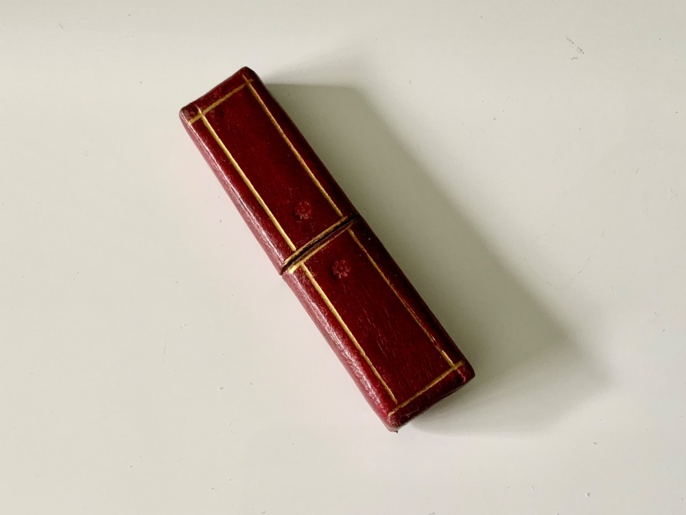 An antique folding veterinary lancet with tortoiseshell handles and a short steel blade alongside a red gilt-tooled leather case. View II