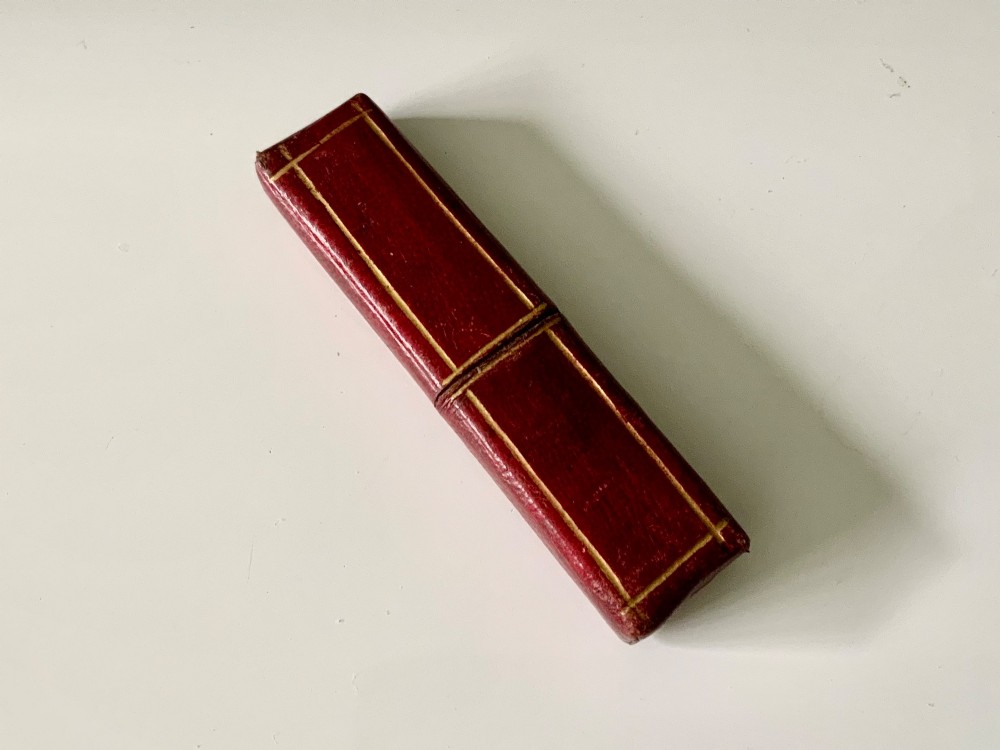 An antique folding veterinary lancet with tortoiseshell handles and a short steel blade alongside a red gilt-tooled leather case. View III
