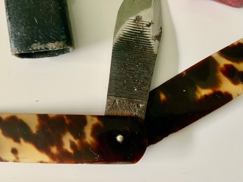 An antique folding veterinary lancet with tortoiseshell handles and a short steel blade alongside a red gilt-tooled leather case. View VI