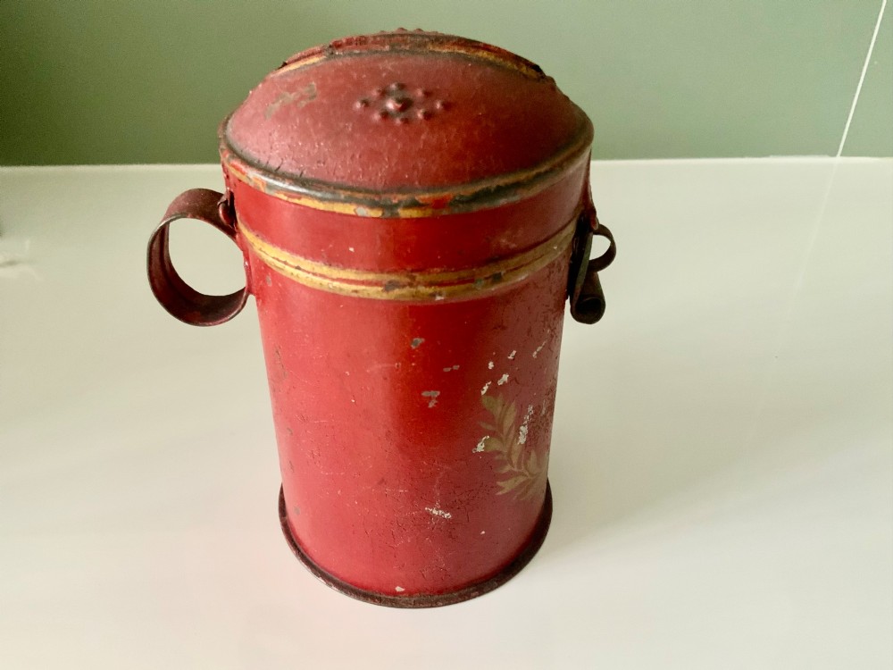 A cylindrical red painted toleware money box dated 1818 featuring a domed top with coin slot, metal latch, and gilded leaf decoration. View II