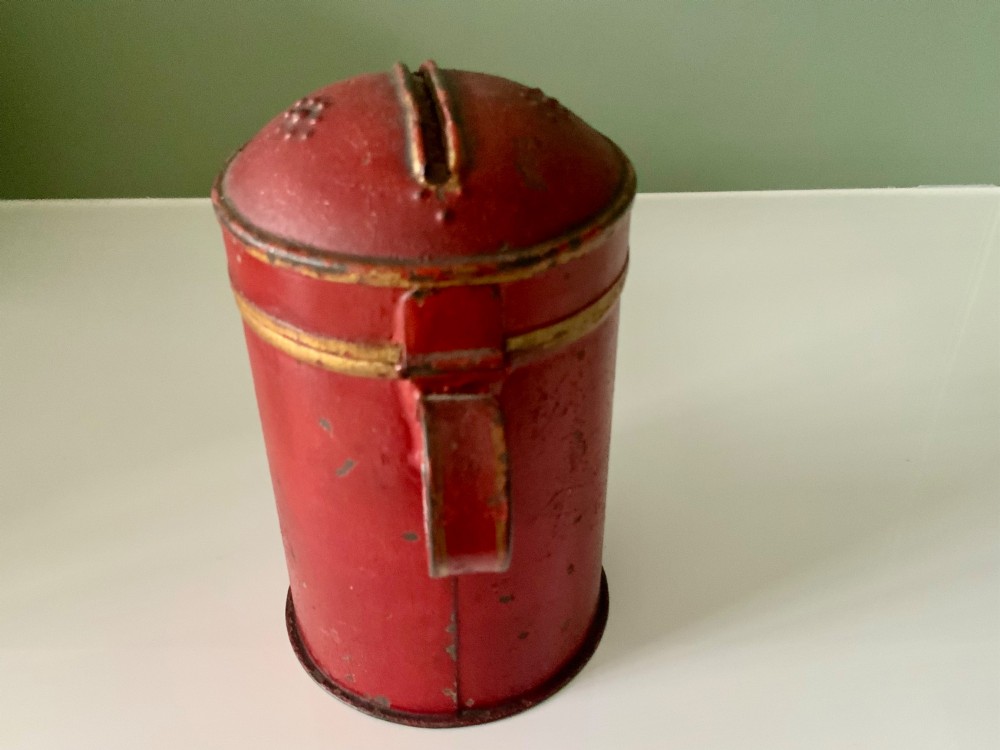 A cylindrical red painted toleware money box dated 1818 featuring a domed top with coin slot, metal latch, and gilded leaf decoration. View IV