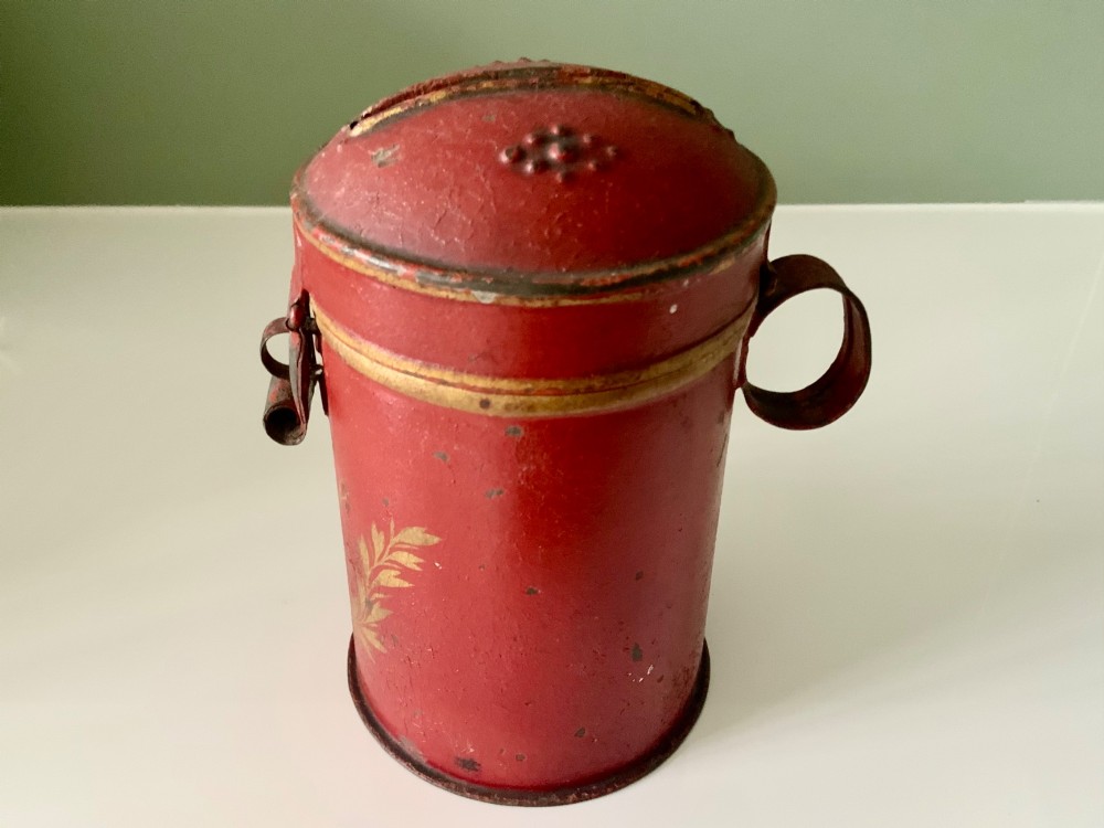 A cylindrical red painted toleware money box dated 1818 featuring a domed top with coin slot, metal latch, and gilded leaf decoration. View V