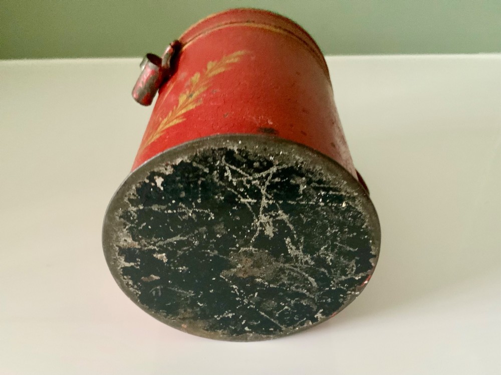 A cylindrical red painted toleware money box dated 1818 featuring a domed top with coin slot, metal latch, and gilded leaf decoration. View VI