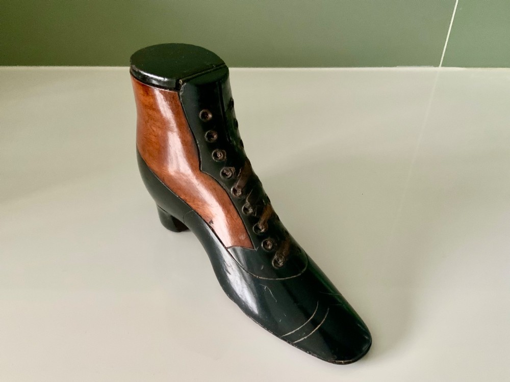 A carved wooden snuff box formed in the shape of a Victorian laced boot with polished black and natural timber finishes.