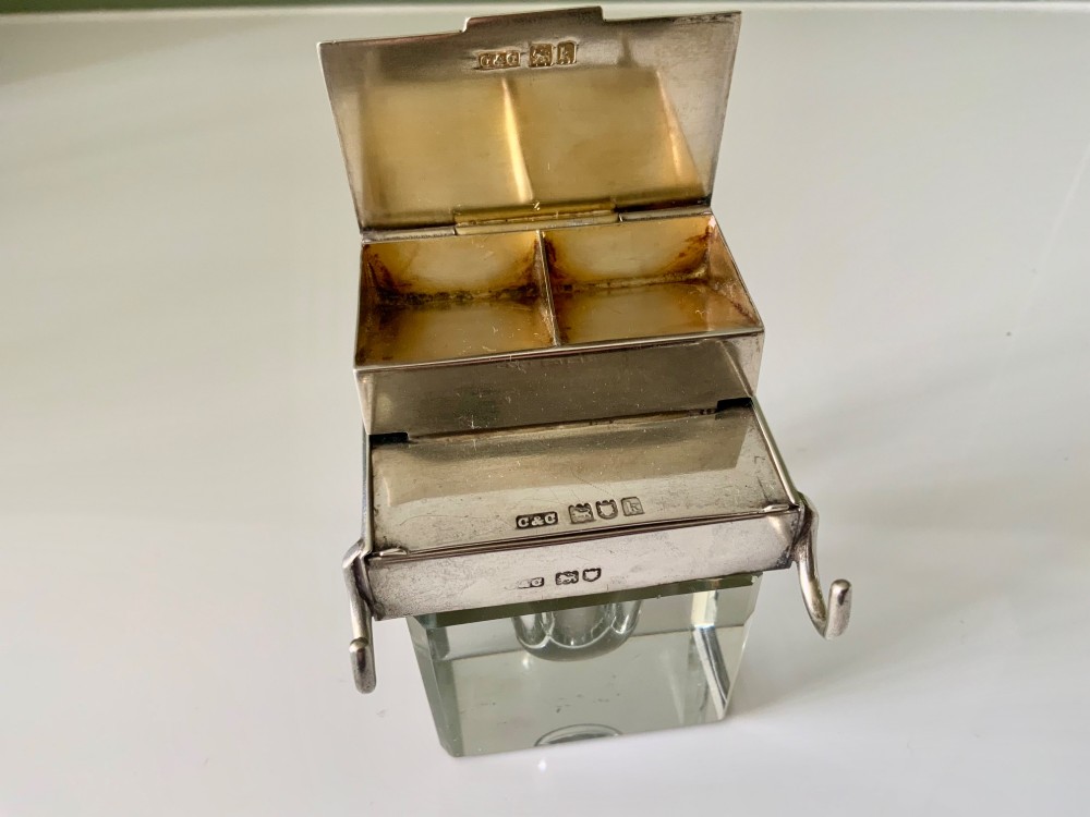 A square clear glass inkwell featuring a hallmarked sterling silver hinged lid, integrated stamp compartment, and side pen rests. View II