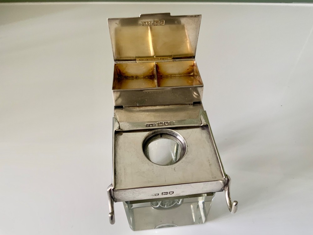 A square clear glass inkwell featuring a hallmarked sterling silver hinged lid, integrated stamp compartment, and side pen rests. View III